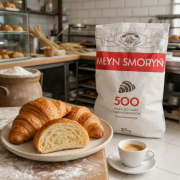 Mąka-500-do-ciast-laminowanych-złociste croissanty-ze-szczegółowym-przekrojem-o-strukturze-plastra-miodu-filiżankę-espresso-i-oprószony-drewniany-blat.png